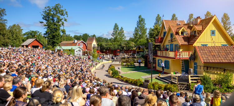 Bild från teaterföreställning om Pippi Långstrump med Villa villekulla i bakgrunden och mycket publik framför scenen på Astrid Lindgrens värld.